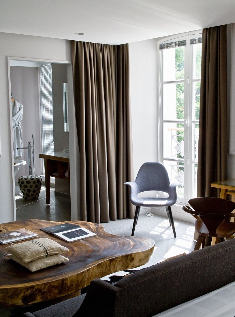 Massive wooden table with live edge and fifties-style chair next to window in interior with traditional character