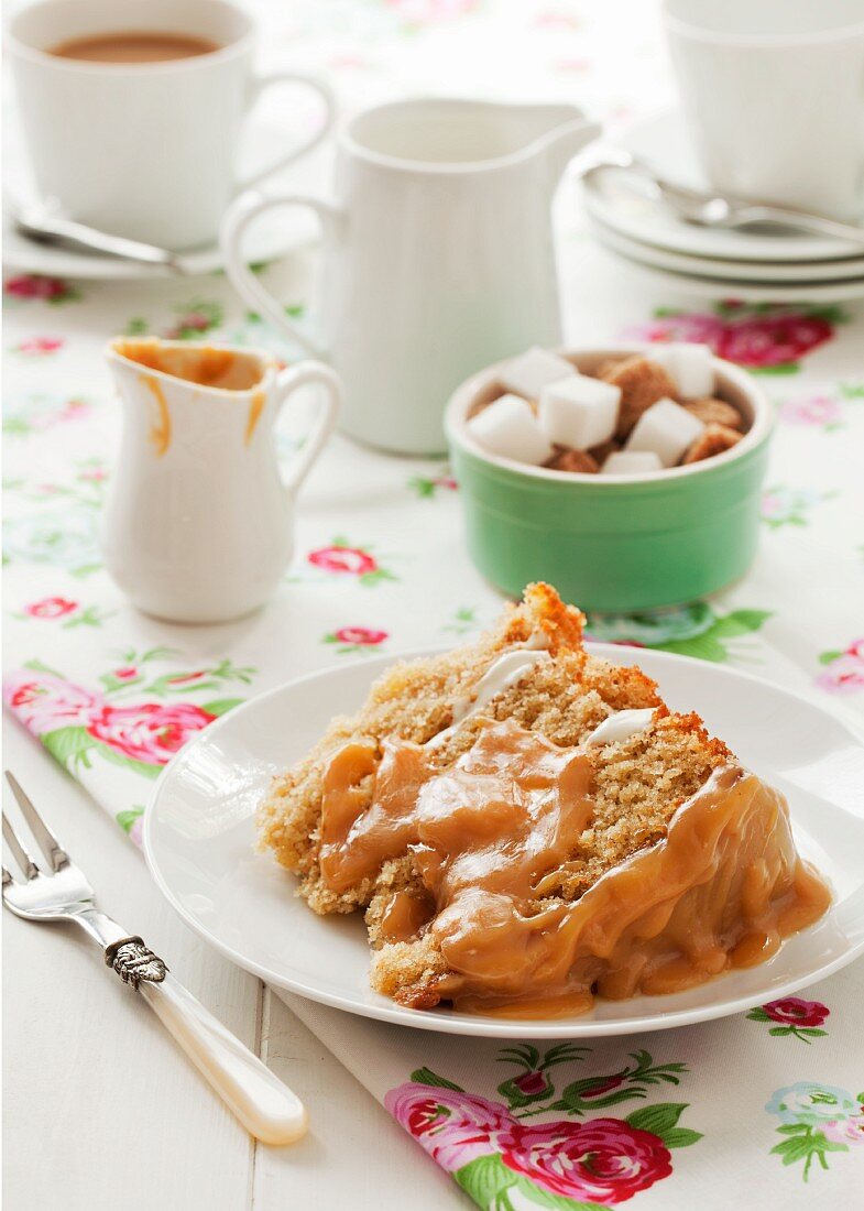 Ein Stück Apfel-Zimt-Biskuitkuchen mit Karamellglasur, Würfelzucker und Tee