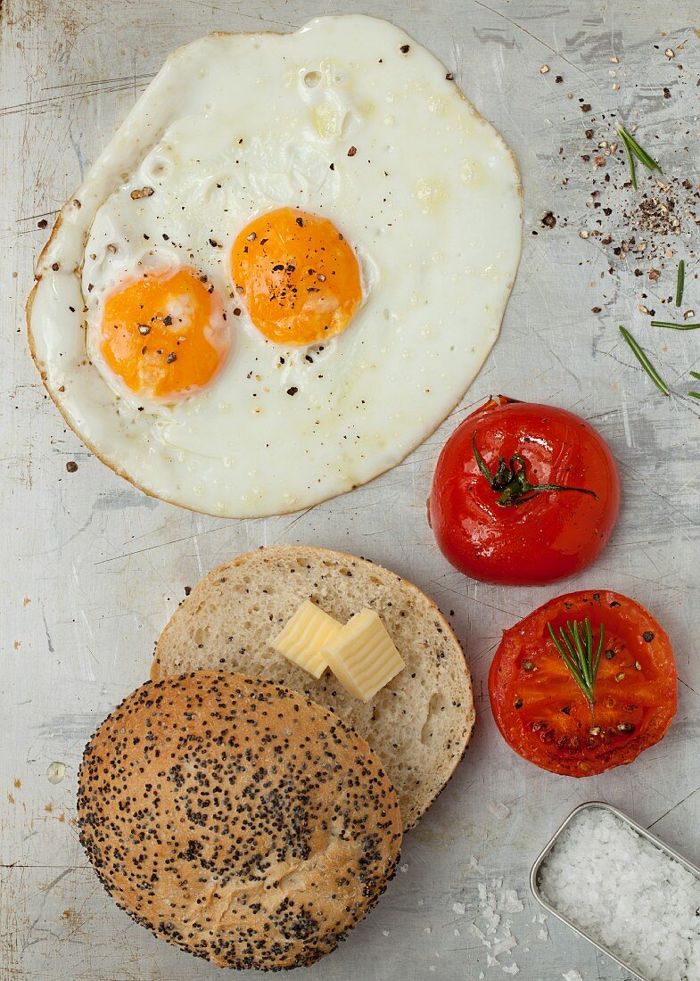 A fried egg with tomatoes and a poppyseed roll with butter