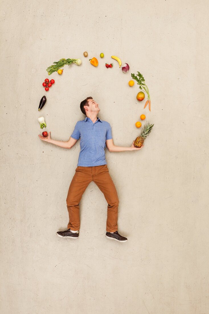Mann jongliert mit Obst und Gemüse