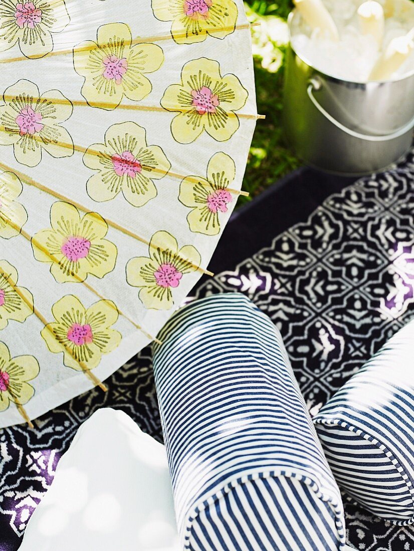 White and blue striped bolster on Moroccan blanket below paper parasol