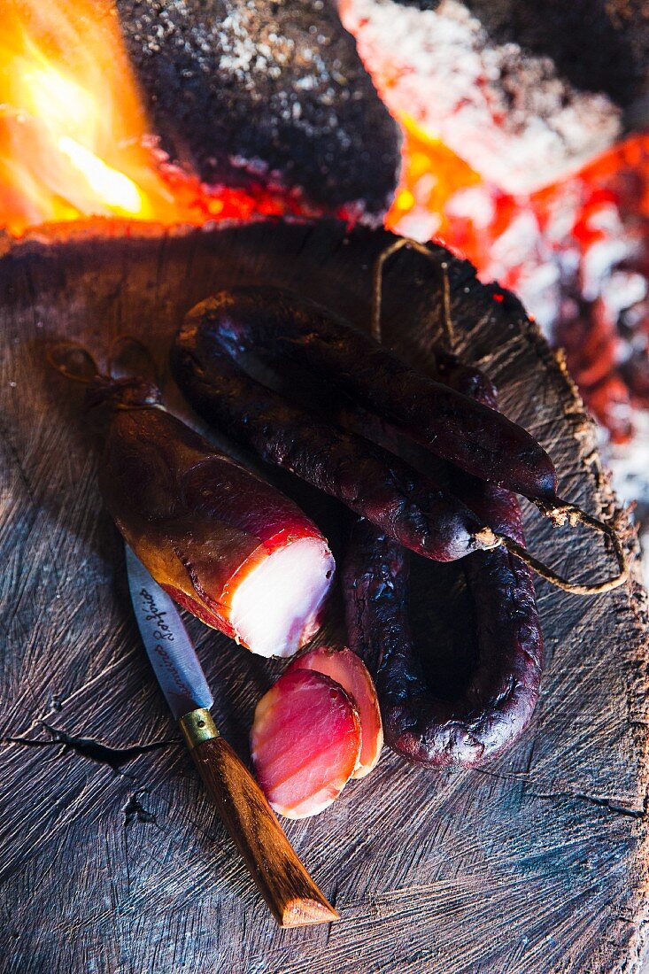 Gegrillte Chorizo auf Baumstamm neben Lagerfeuer