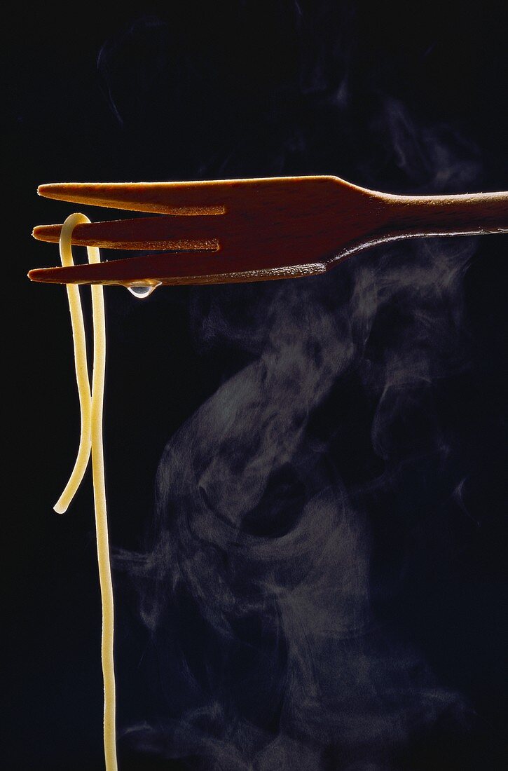 Eine gekochte Spaghetti-Nudel hängt von einer Holzgabel