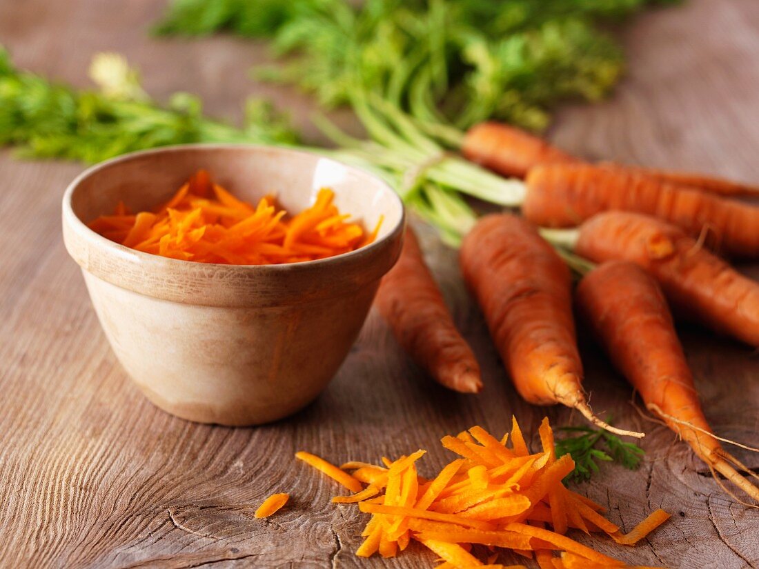 Fresh organic carrots next to a bowl of grated carrots