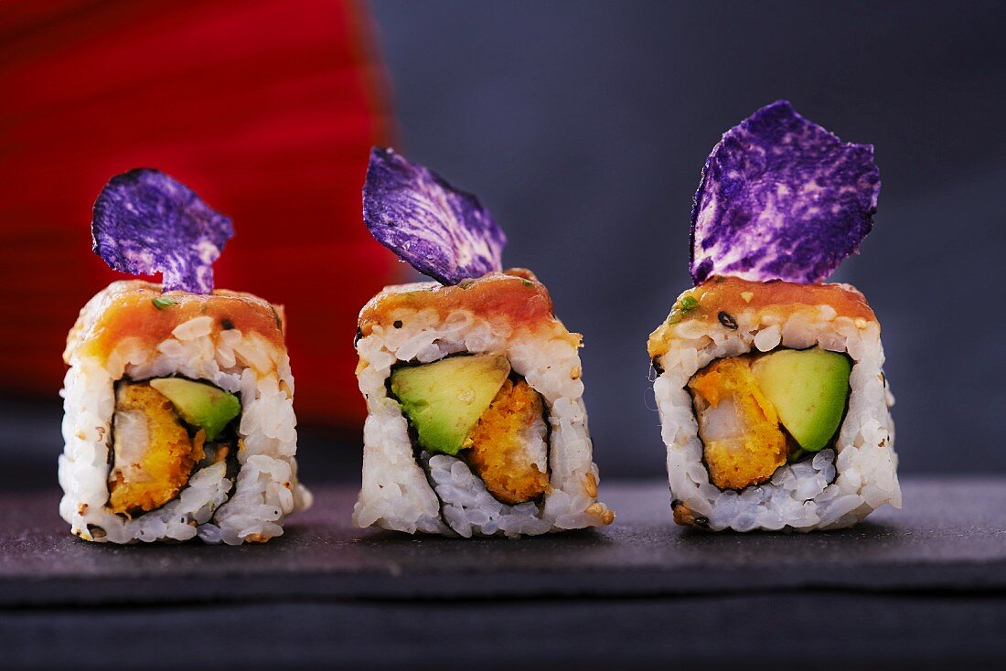 Three sushi rolls with salmon, avocado and purple potato crisps