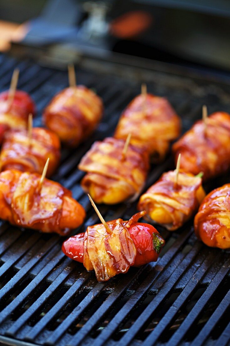 Stuffed mini peppers wrapped in bacon on a barbecue