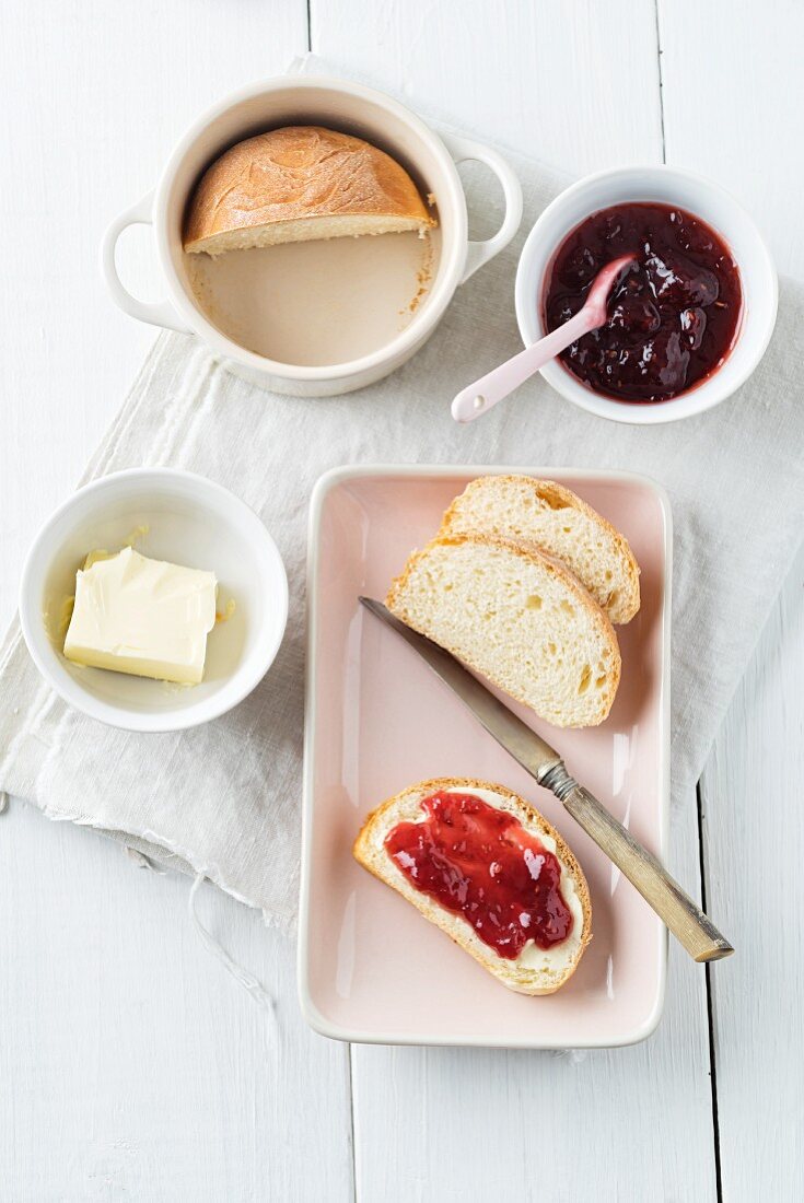 A mini loaf of white bread baked in a cup and served with butter and strawberry jam