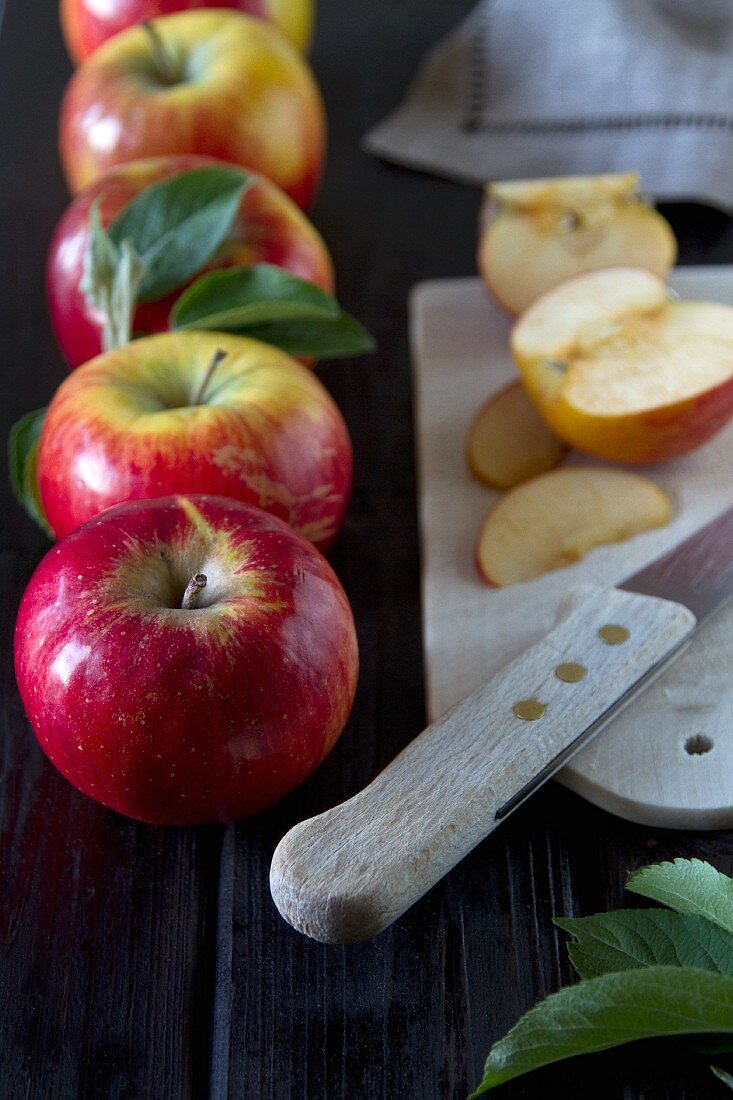 Äpfel mit Blättern, geschnitten auf Brettchen mit Messer