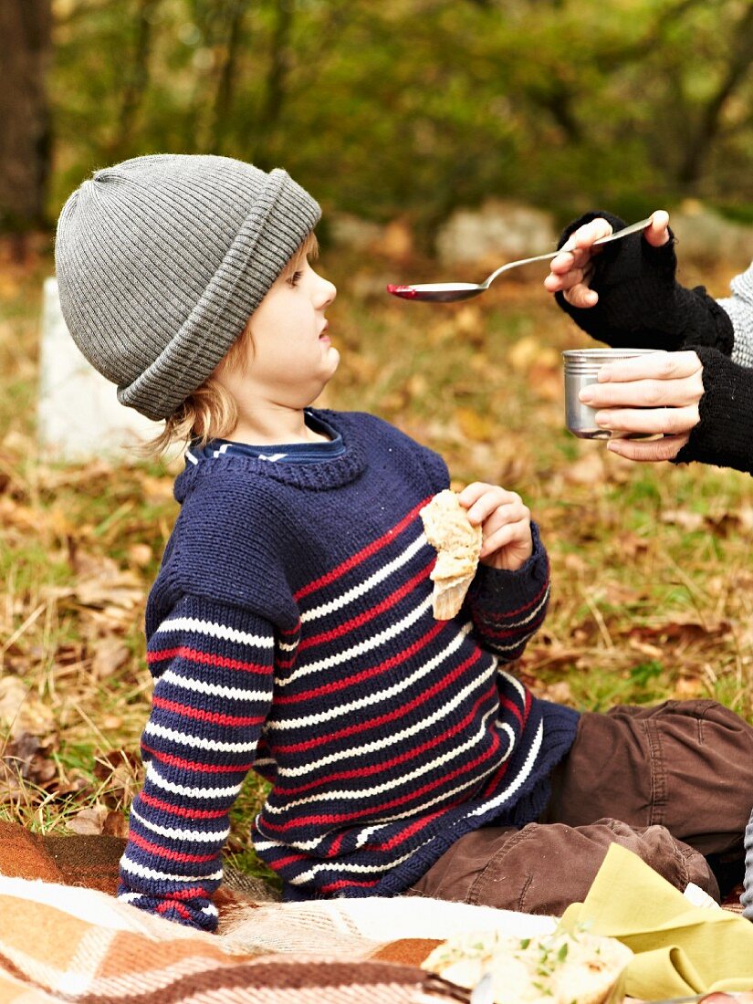 Frau füttert Kind mit Rote-Bete-Suppe beim Herbstpicknick