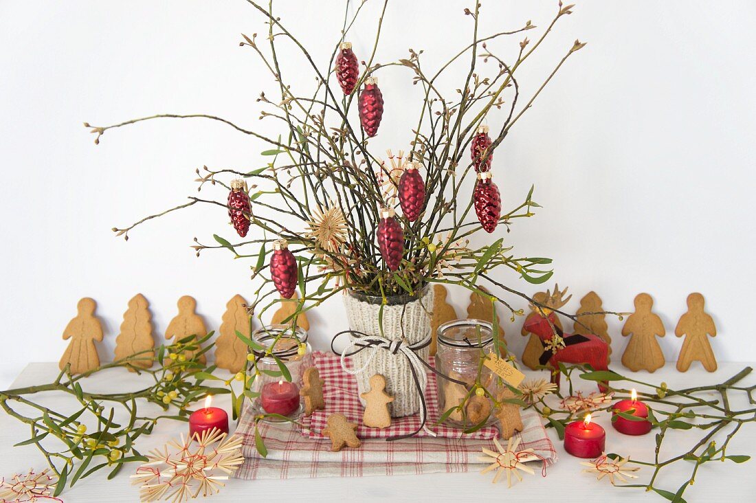 Weihnachtsstrauss mit roten Tannenzapfen; daneben Glasschmuck, Strohsterne, Mispeln und Spekulatius