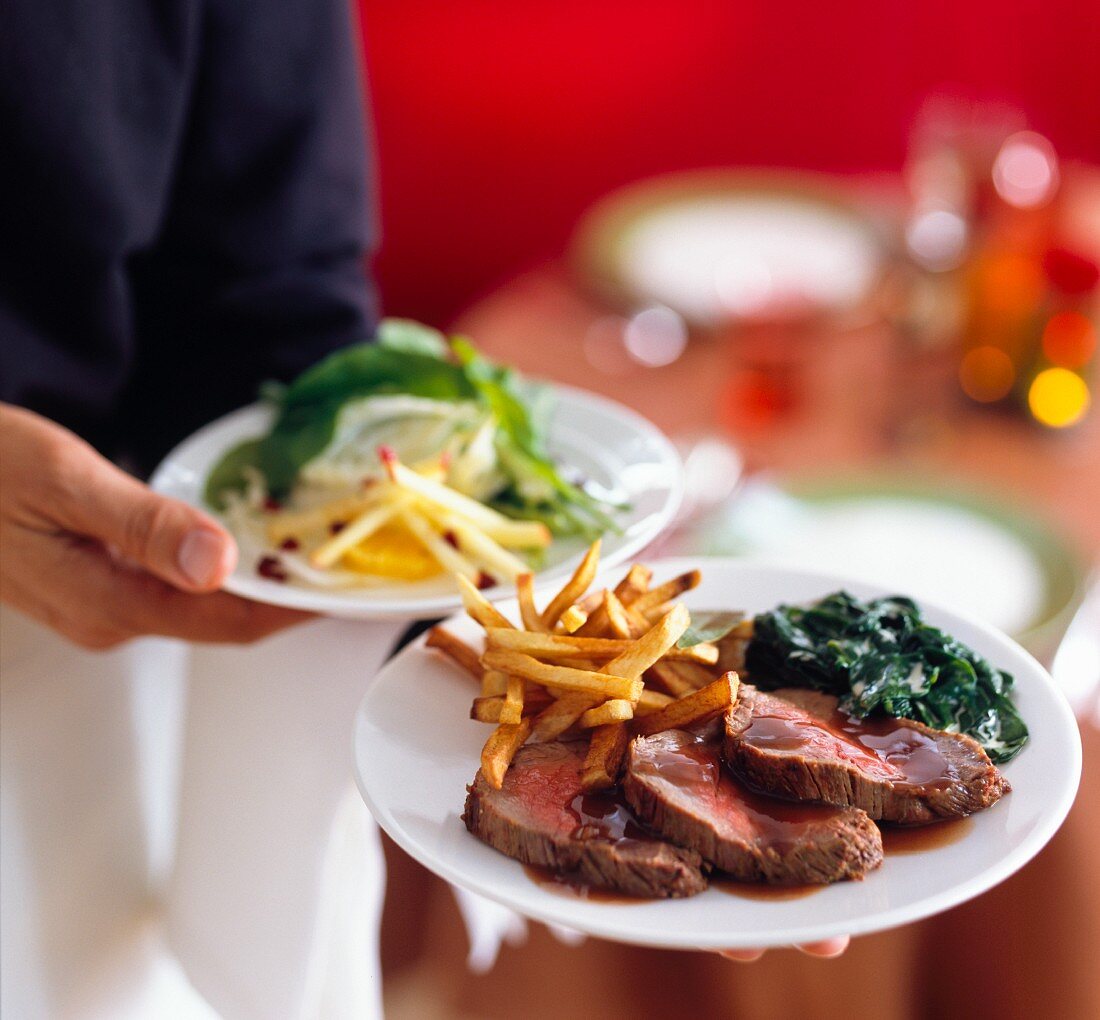 A waiter serving beef tenderloin with fries and spinach