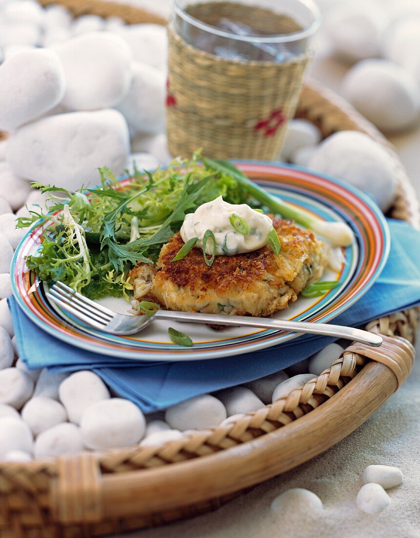 A crabcake and salad on a plate on the beach
