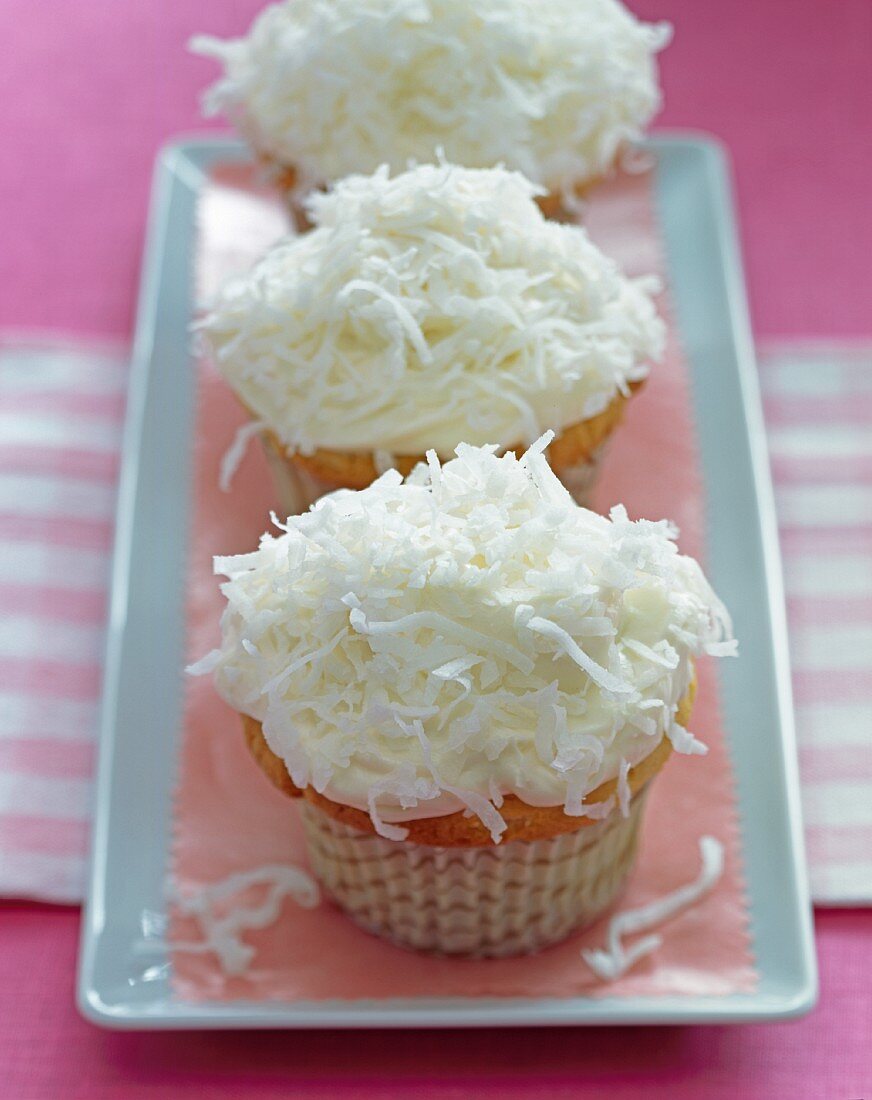 Three cupcakes decorated with vanilla frosting and grated coconut