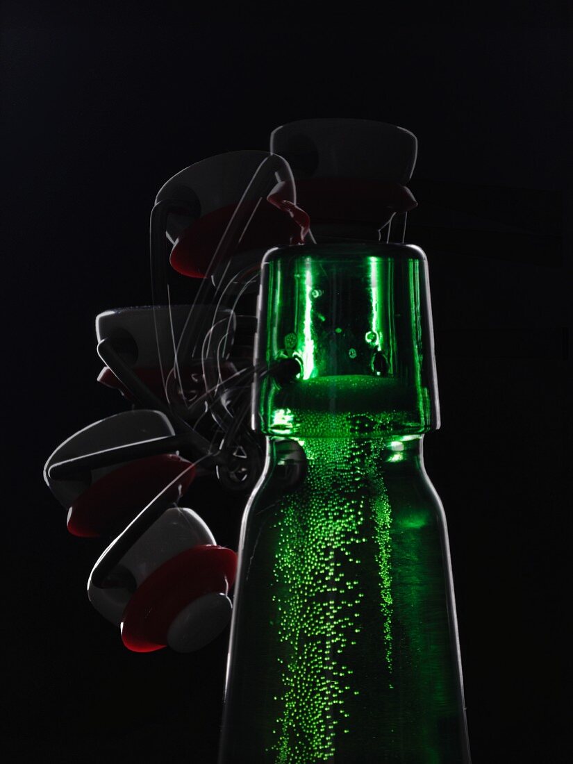 A green beer bottle with a flip-top lid backlit against a black background being opened (multiple expose)