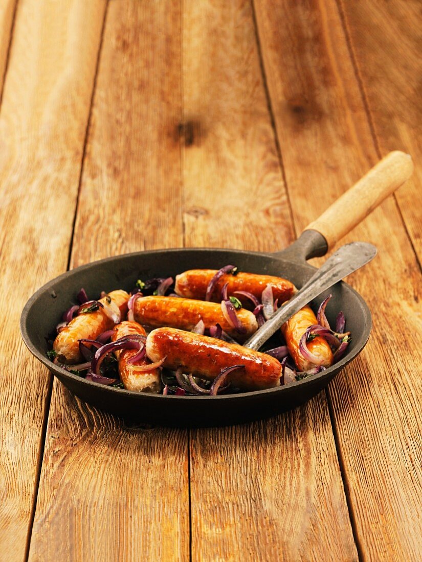 Sausages with red onions and thyme in a pan