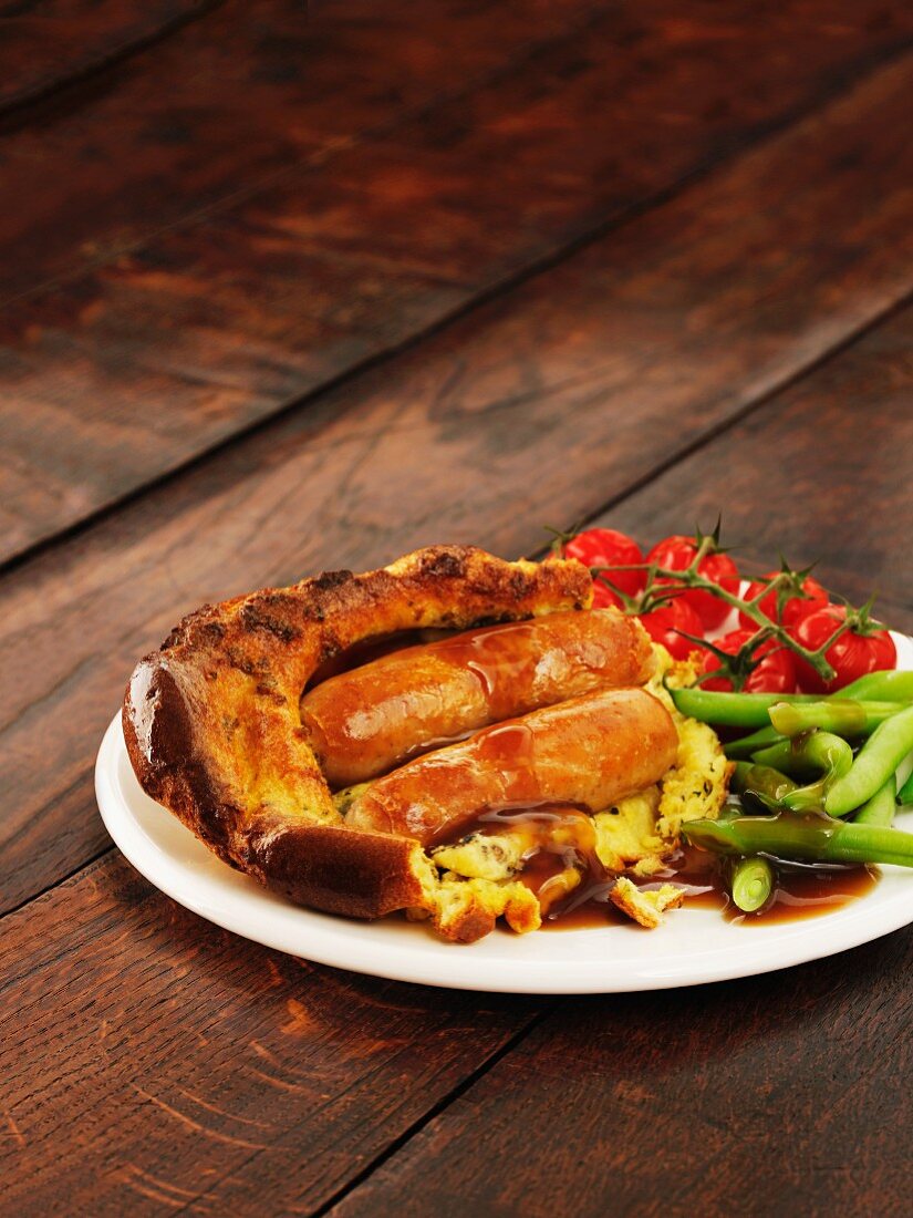 Toad in the hole (Bratwürstchen im Teig gebacken) mit Bohnen und Tomaten