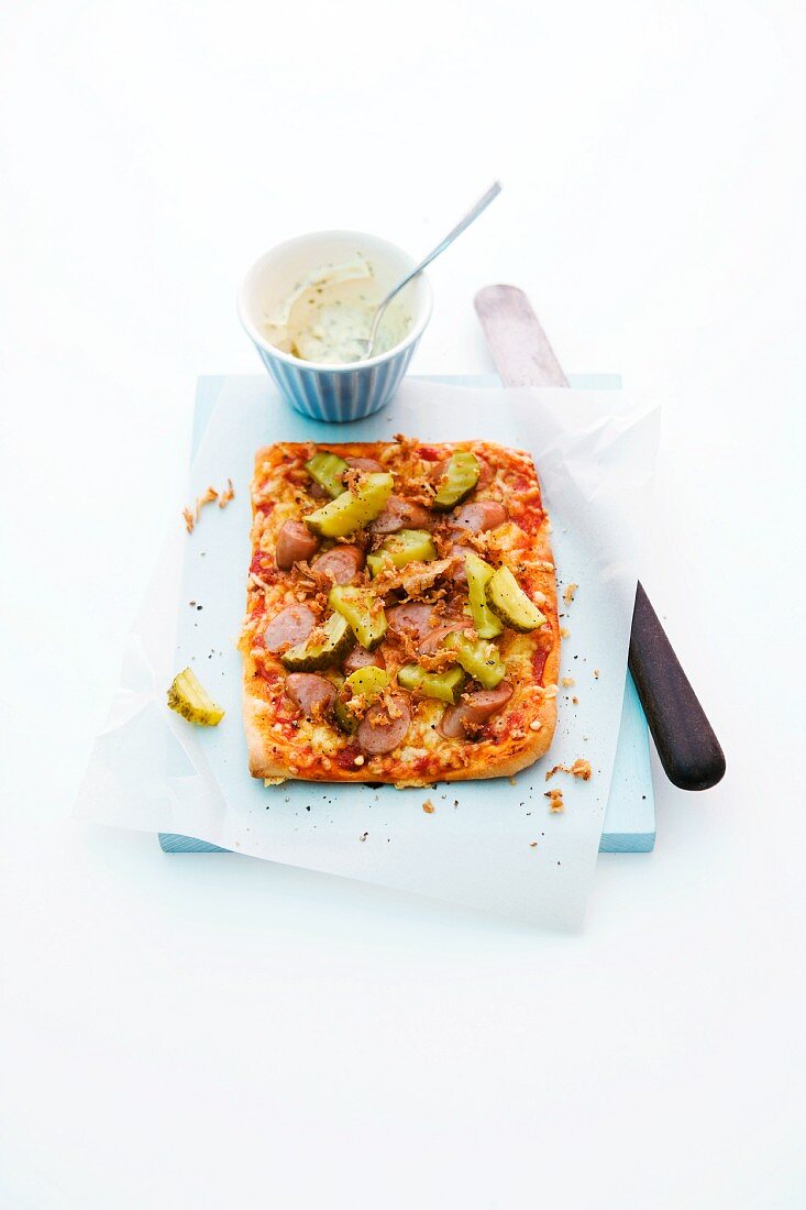 A slice of pizza topped with hot dog sausages and gherkins