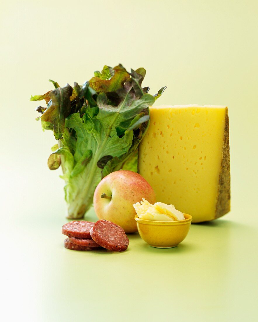 An arrangement of cheese, salami, an apple and an oak leaf