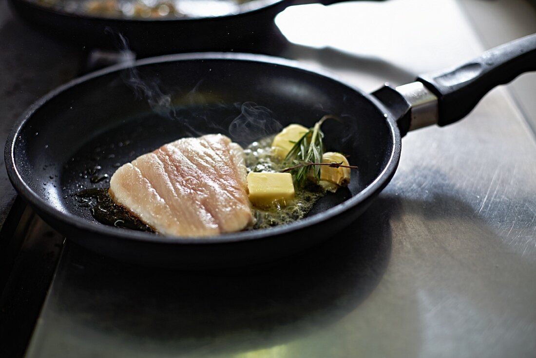 Fish fillet with butter and herbs in a pan