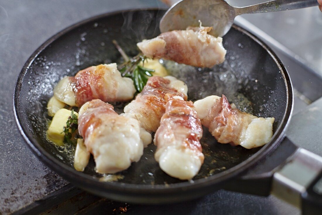 Fischfilets im Speckmantel werden in der Pfanne gebraten