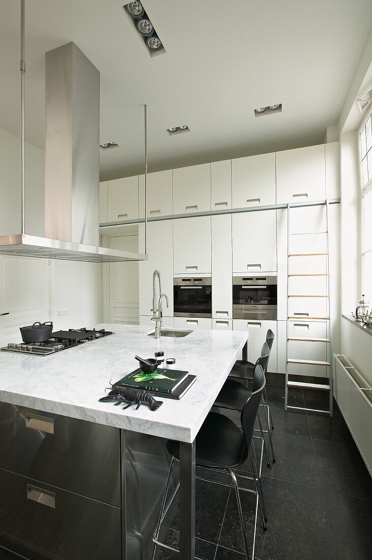 Kitchen island with marble worksurface in white fitted kitchen with black floor tiles