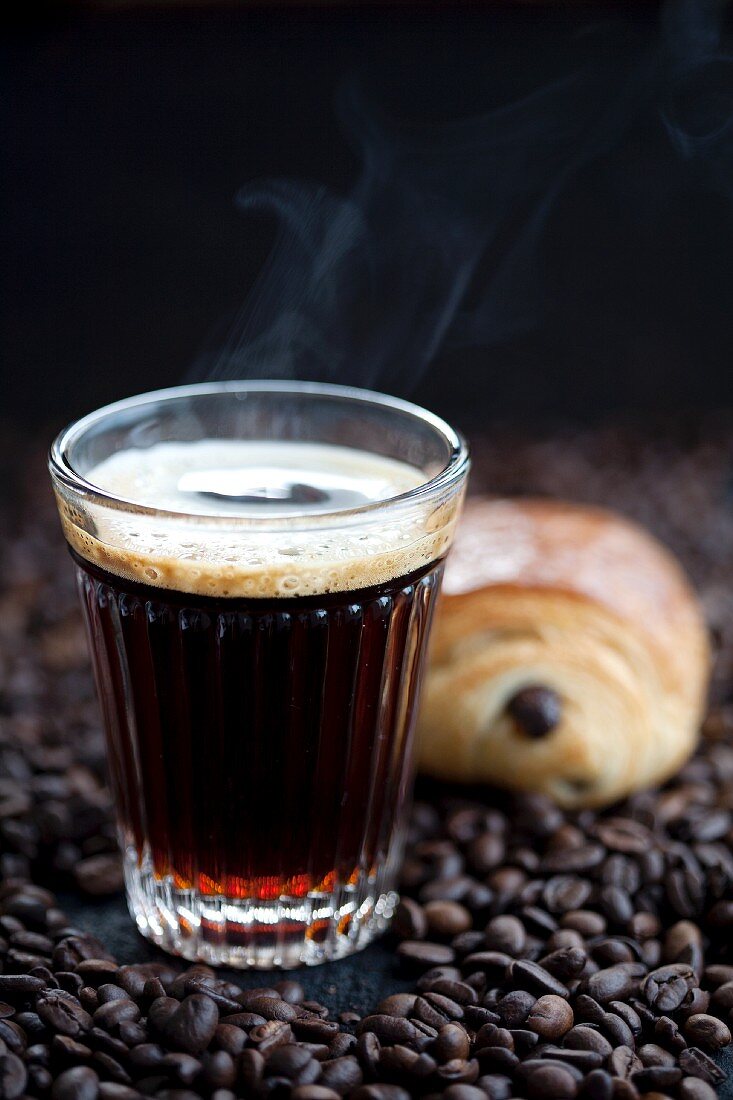 Coffee and a chocolate croissant on coffee beans