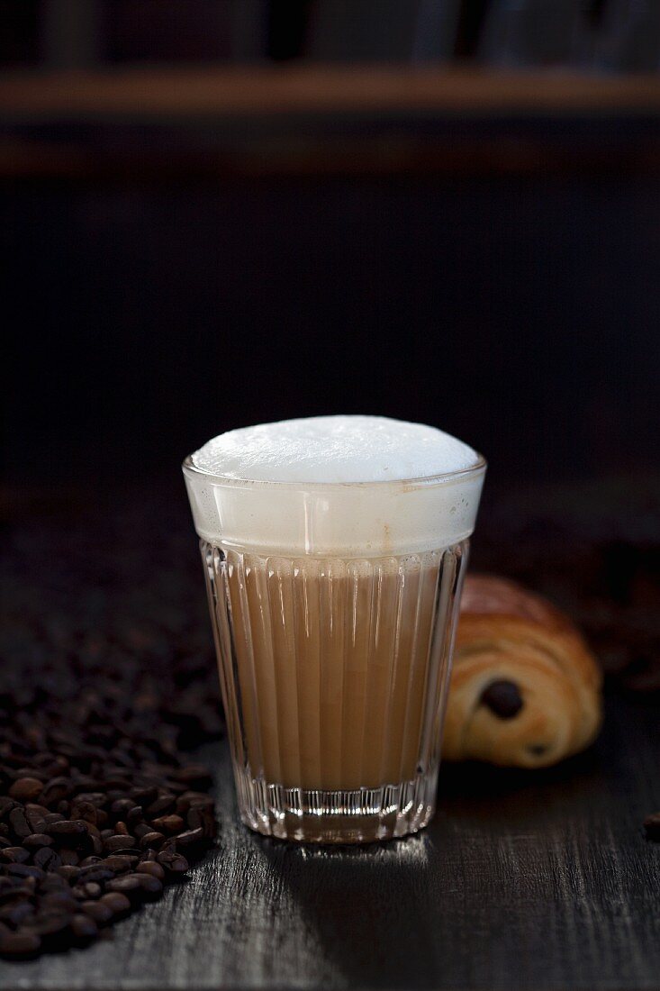 A latte macchiato, chocolate croissant and coffee beans