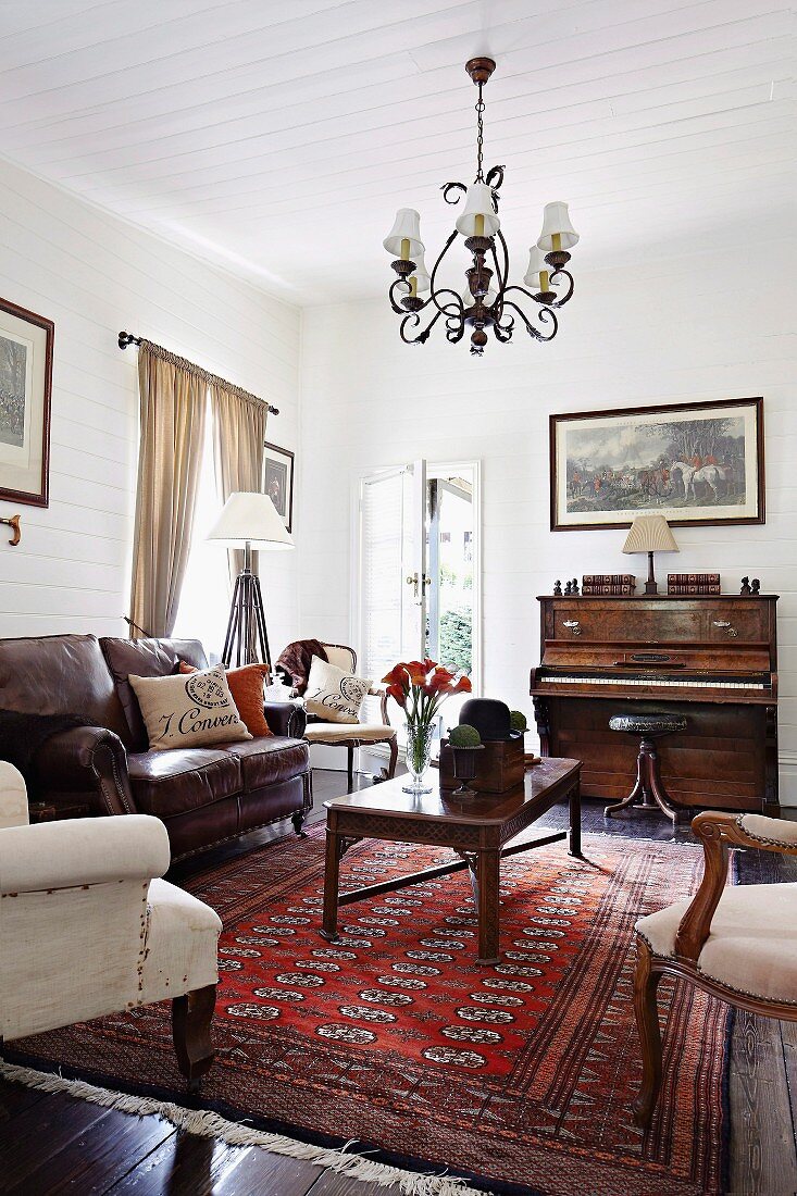 Leather sofa, antique armchairs, wooden coffee table on Oriental rug and piano in traditional, rustic living room