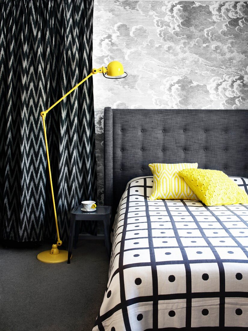 Doppelbett mit grau gepolstertem Kopfteil neben gelber Retro Stehleuchte vor Wand mit wolkiger Mustertapete