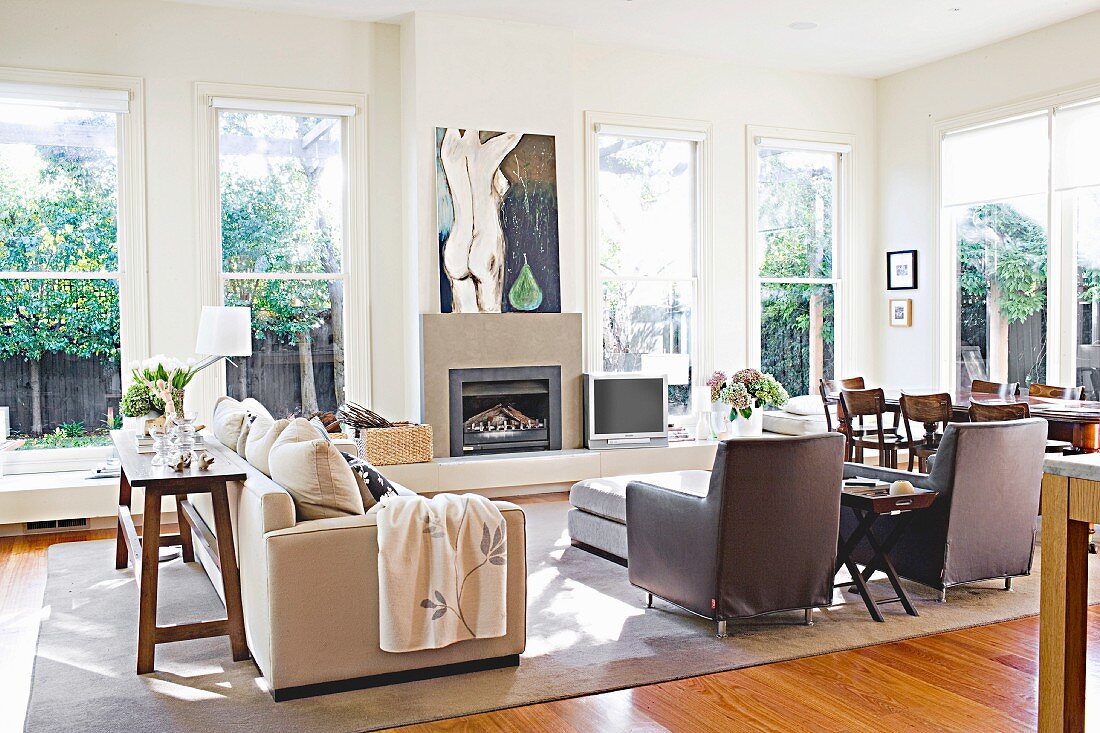 Female nude painting above modern fireplace flanked by windows with low continuous windowsill in light-flooded interior