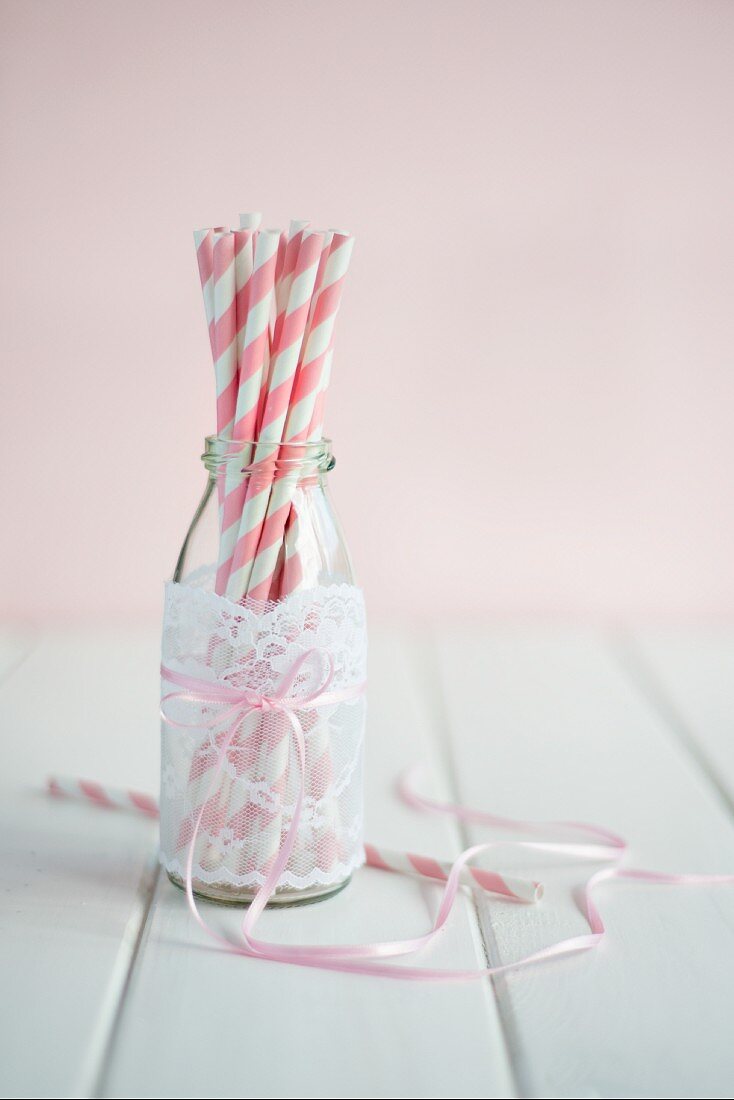 Straws in an empty smoothie bottle decorated with a piece of lace