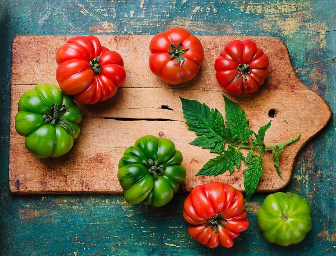 Green and red beefsteak tomatoes with leaves on a chopping board