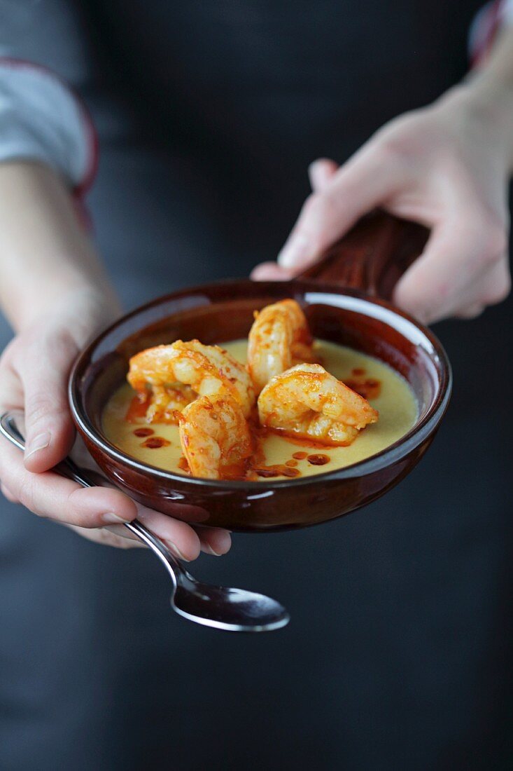 A person holding a pan of fried prawns in cheese sauce