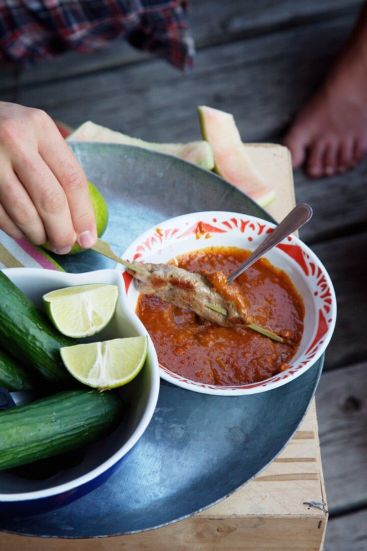 A satay skewer being dipped into sauce