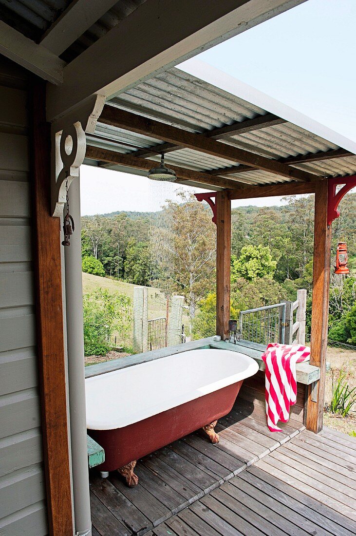 Vintage Badewanne auf Holzboden einer überdachten Terrasse und Blick in mediterrane Landschaft