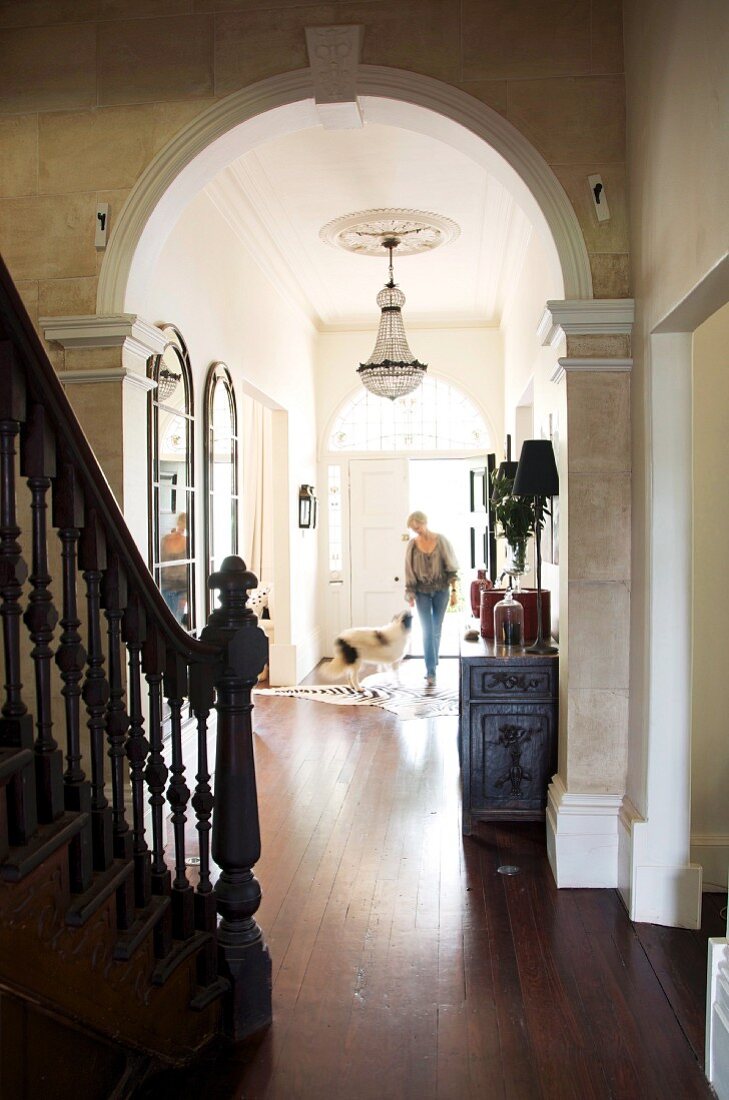 Blick vom Treppenraum durch Rundbogen auf Frau mit Hund in schmalem Gang einer herrschaftlichen Villa