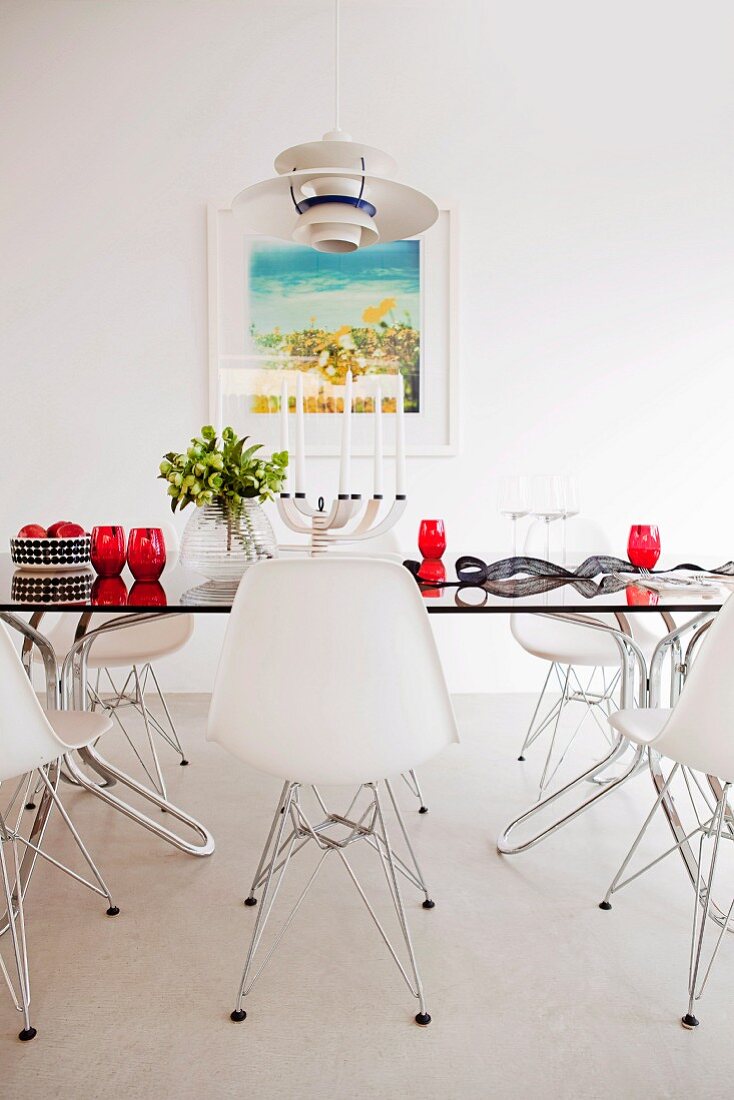Classic, white shell chairs around glass table with red glasses in minimalist dining room