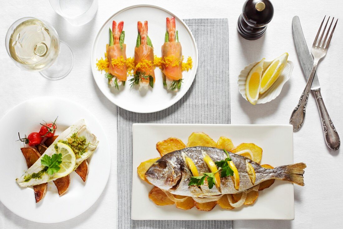 Drei verschiedene Fischgerichte mit Zitronen und Weißwein