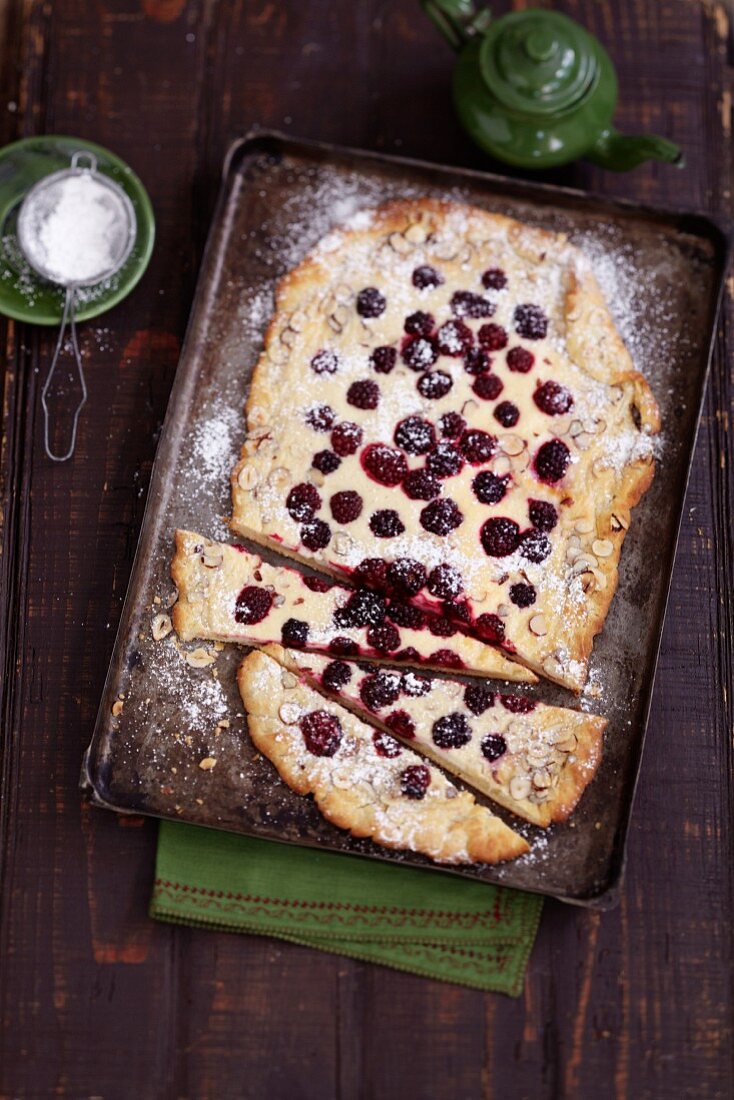 Blackberry and sour cream flan dusted with icing sugar on an old baking tray