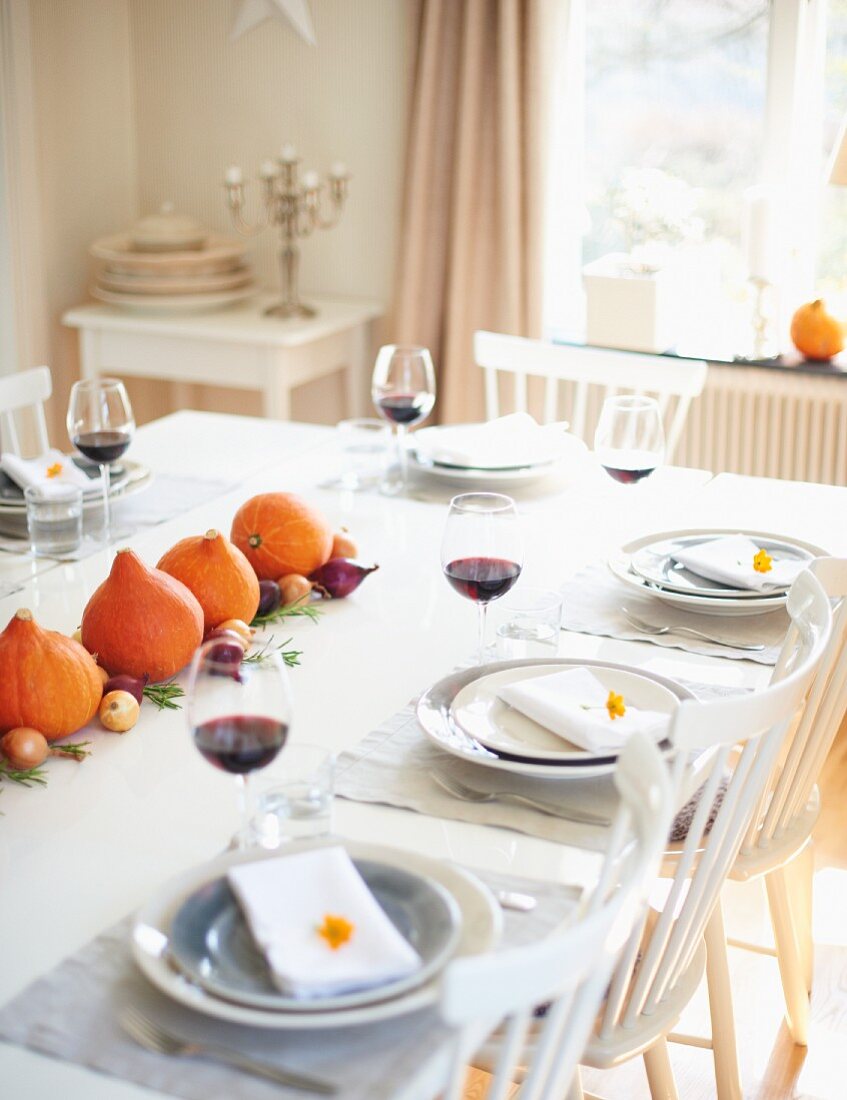 Gedeckter Tisch zu Thanksgiving mit Kürbisdeko, Zwiebeln und Rotwein