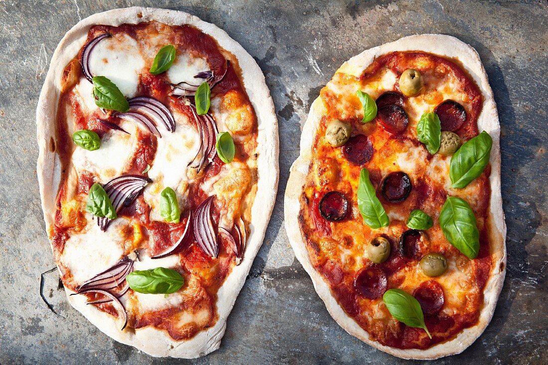 Zwei Steinofenpizza mit Zwiebeln, Salami & Oliven