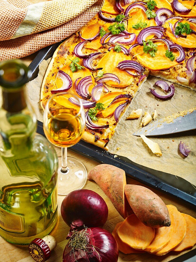 Freshly baked and sliced tarte flambèe with sweet potatoes, red onions, Calvados and parsley on a baking tray