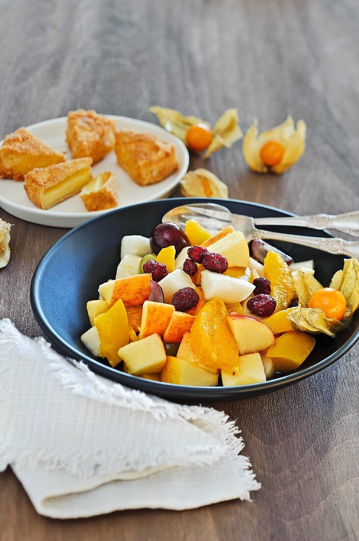 Obstsalat mit Cranberries, Käsekuchen im Hintergrund