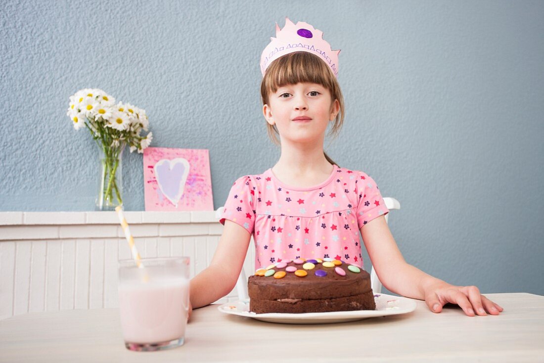 A little girl wearing a crown sitting at a table in front of her birthday cake
