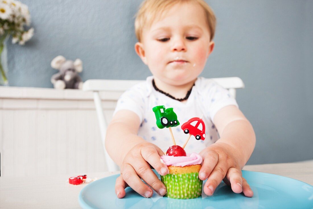 Kleiner Junge spielt mit einem Muffin am Tisch