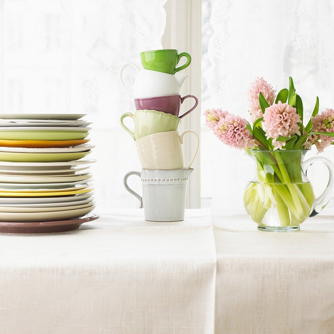 A stack of plates, a stack of cups and a bunch of flowers on a table laid with a white cloth