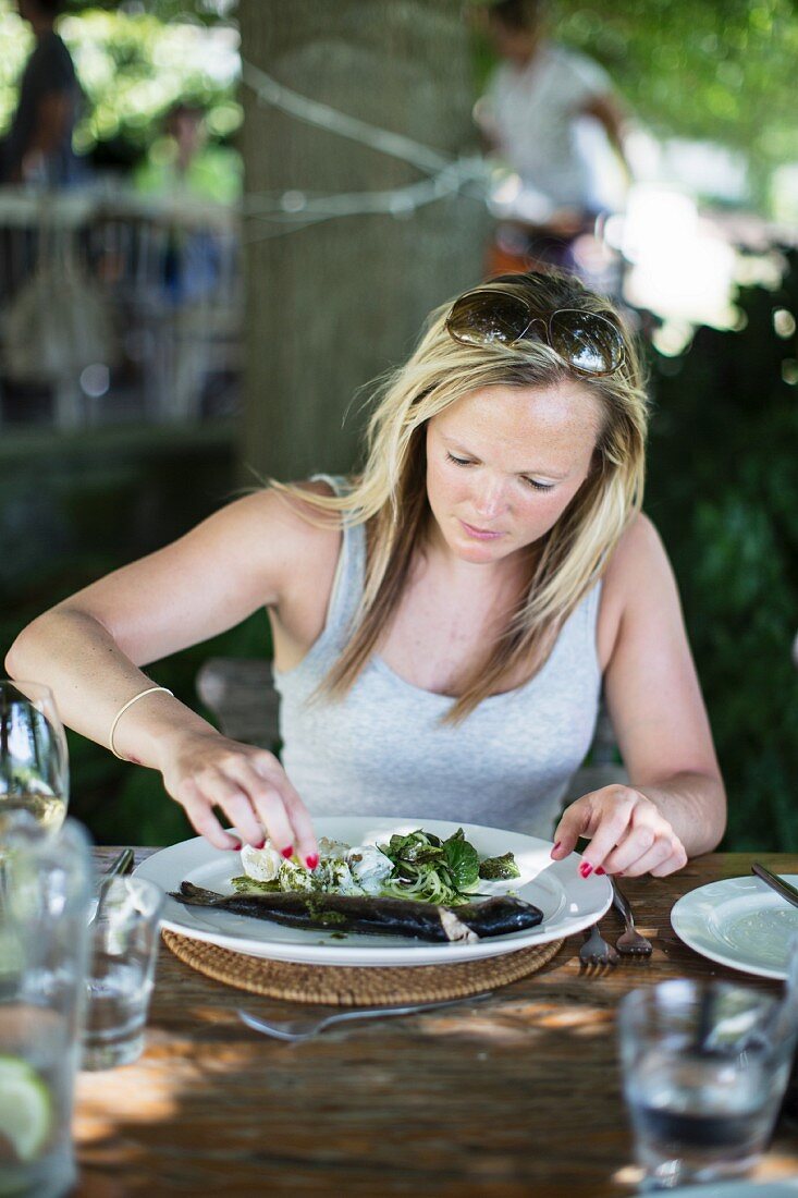 Frau isst Forelle mit Salat im Gartenrestaurant