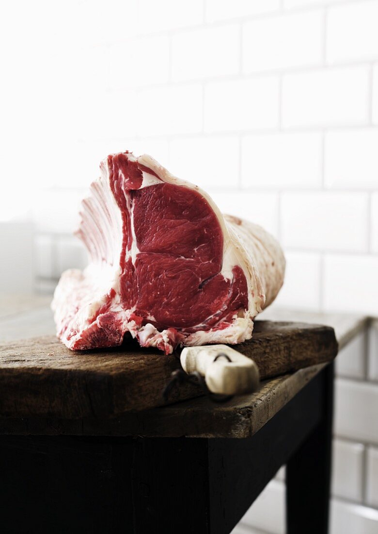 A raw rack of beef with a knife on a chopping board