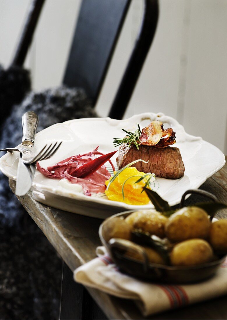 Beef steak with slices of bacon, orange and red cabbage salad