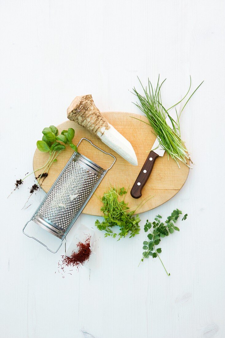 Horseradish root, a grater and herbs on and next to wooden board